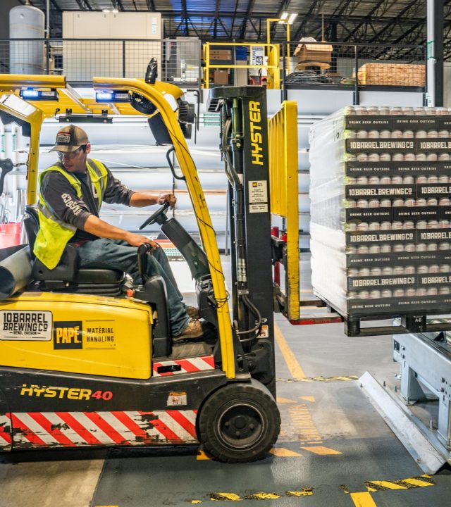 pexels-photo-1267338-1267338 A warehouse worker maneuvers a forklift to transport crates for brewing company storage.